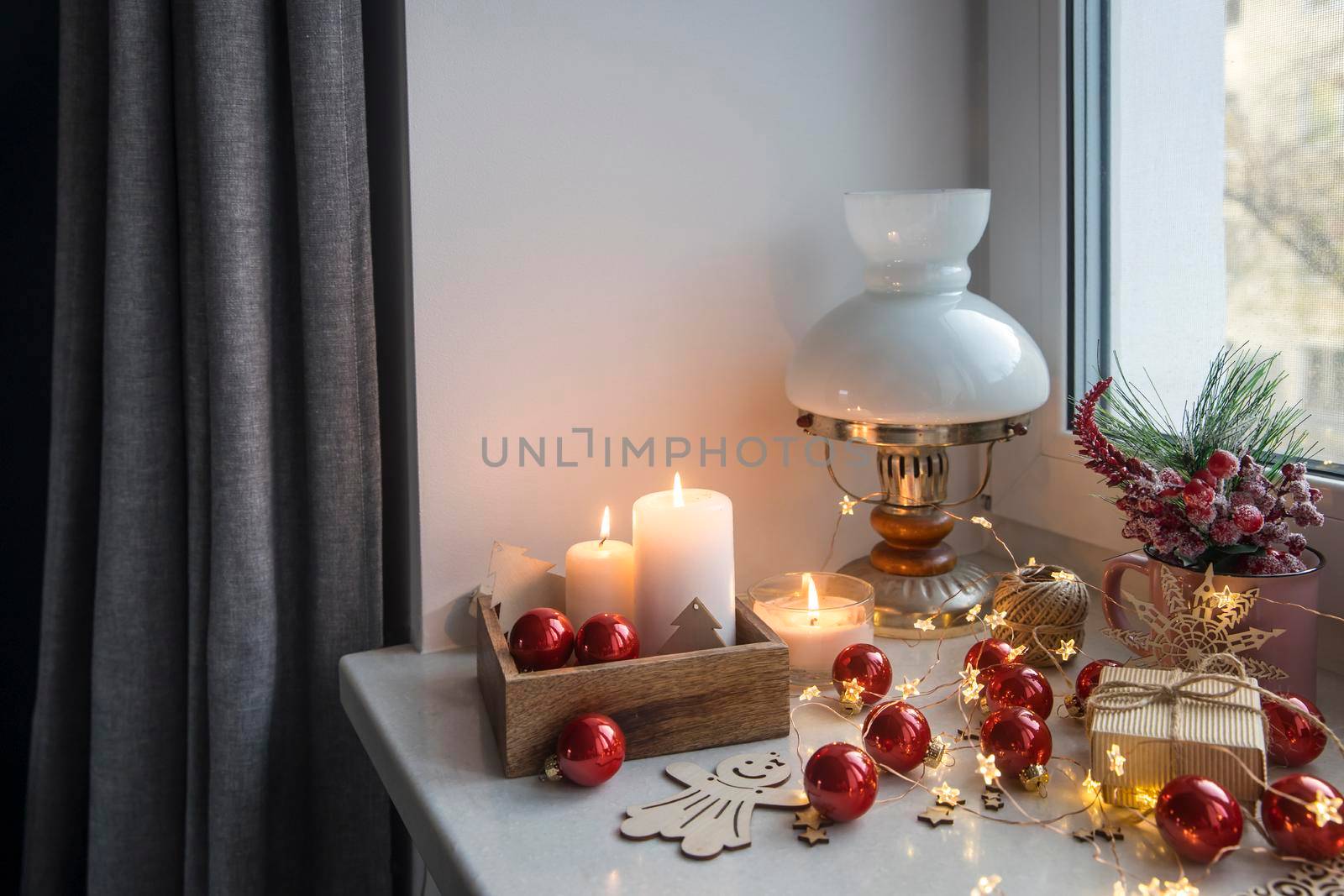 An artificial spruce branch, decorated with ivy leaves, apples and hawthorn berries. Lighted candles in wooden box, red glass balls, winter composition decorates interior on eve of Christmas