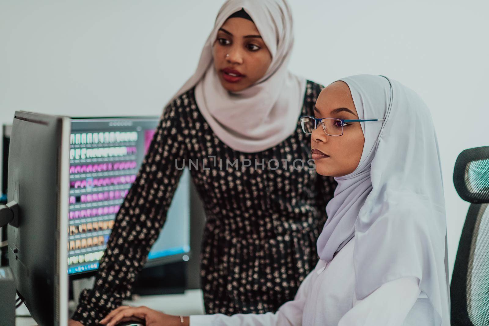 Friends at the office two young Afro American modern Muslim businesswomen wearing scarf in creative bright office workplace with a big screen by dotshock