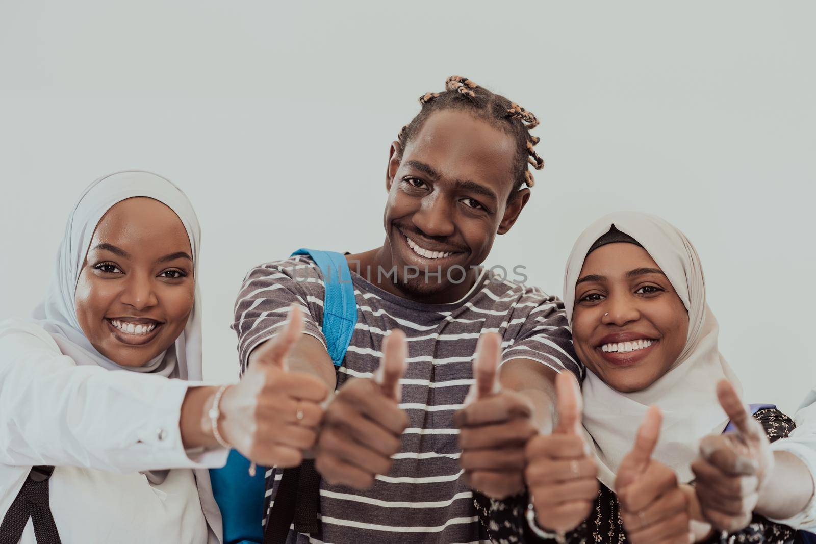 Group portrait of happy African students standing together against a white background and showing ok sign thumbs up girls wearing traditional Sudan Muslim hijab fashion by dotshock