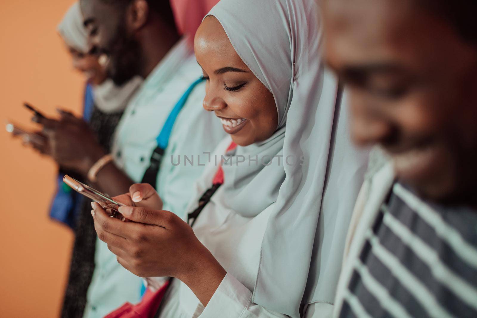 A group of African Muslim students using smartphones while standing in front of a yellow background. High-quality photo