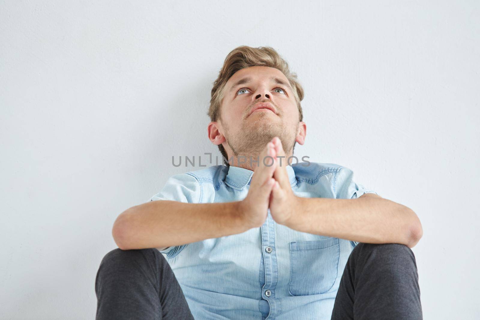 Brutal man in a shirt with short sleeves sitting on floor, his fists clenched, slightly bent, under the gaze of the forehead. High quality photo