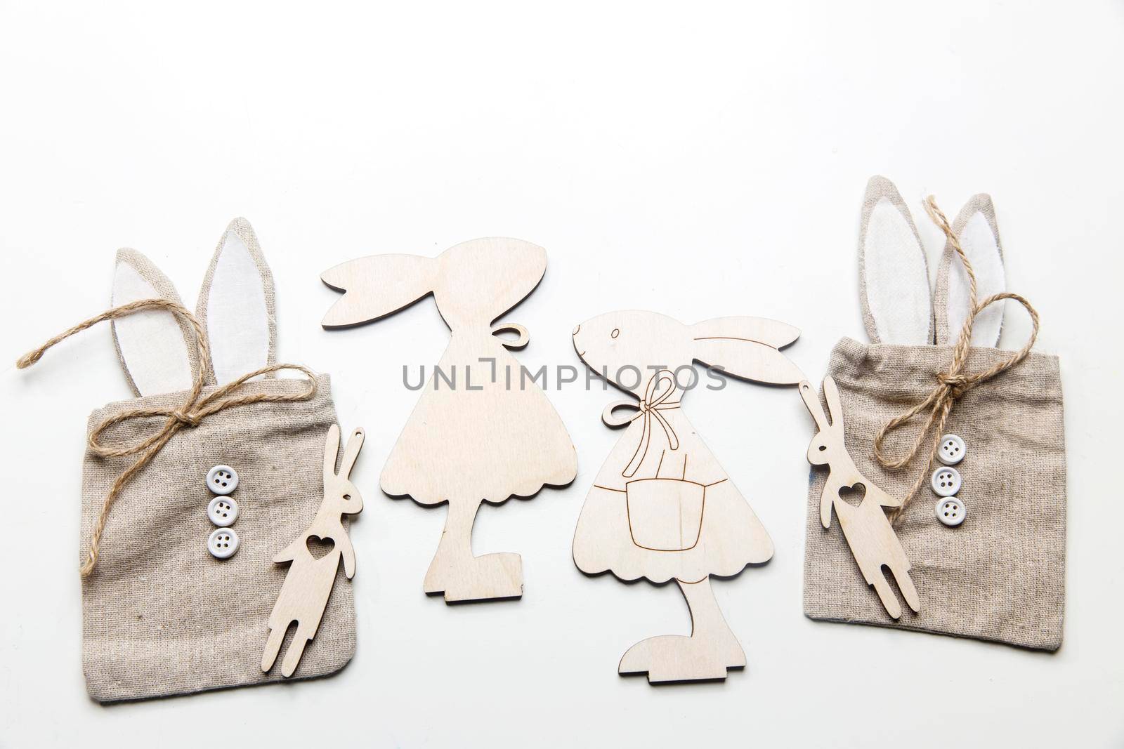 Frame for text. Wooden plywood figures of hares of different sizes, rag canvas bags with ears and buttons, round large beads on a white background by elenarostunova