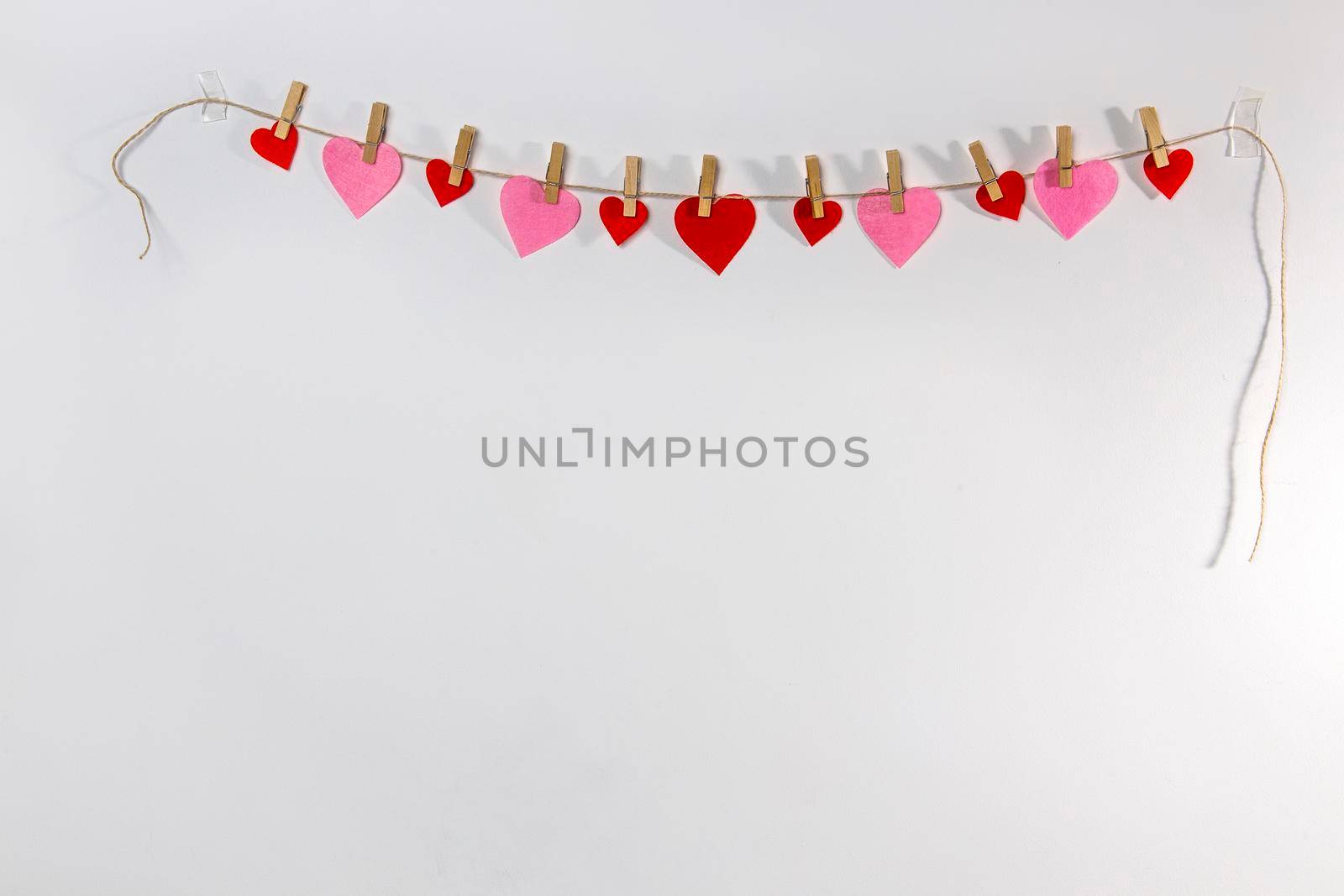 A handmade garland of the hearts is on a white wall. Place for text. Copy space by elenarostunova