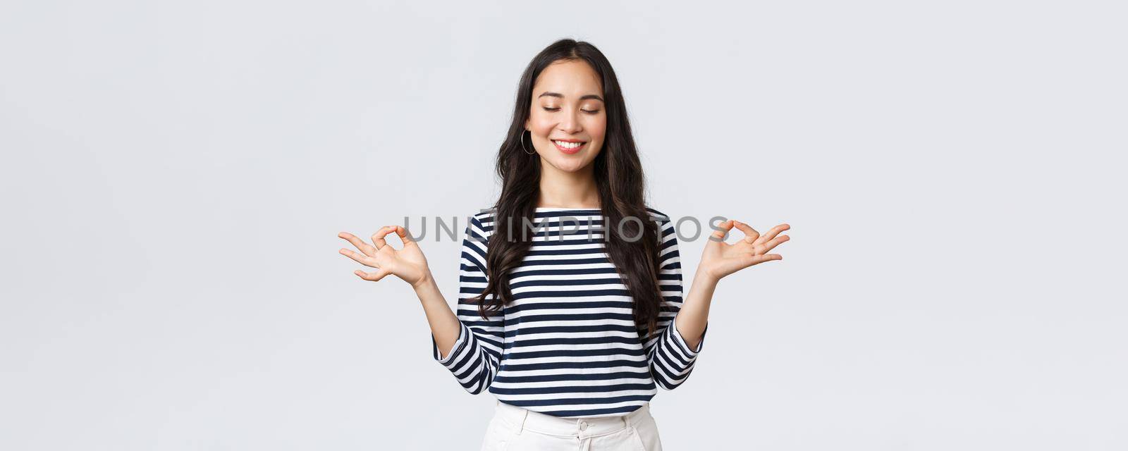 Lifestyle, people emotions and casual concept. Calm happy young woman feeling peaceful during meditation, close eyes and smiling as hold hands in zen nirvana gesture, do yoga exercise.