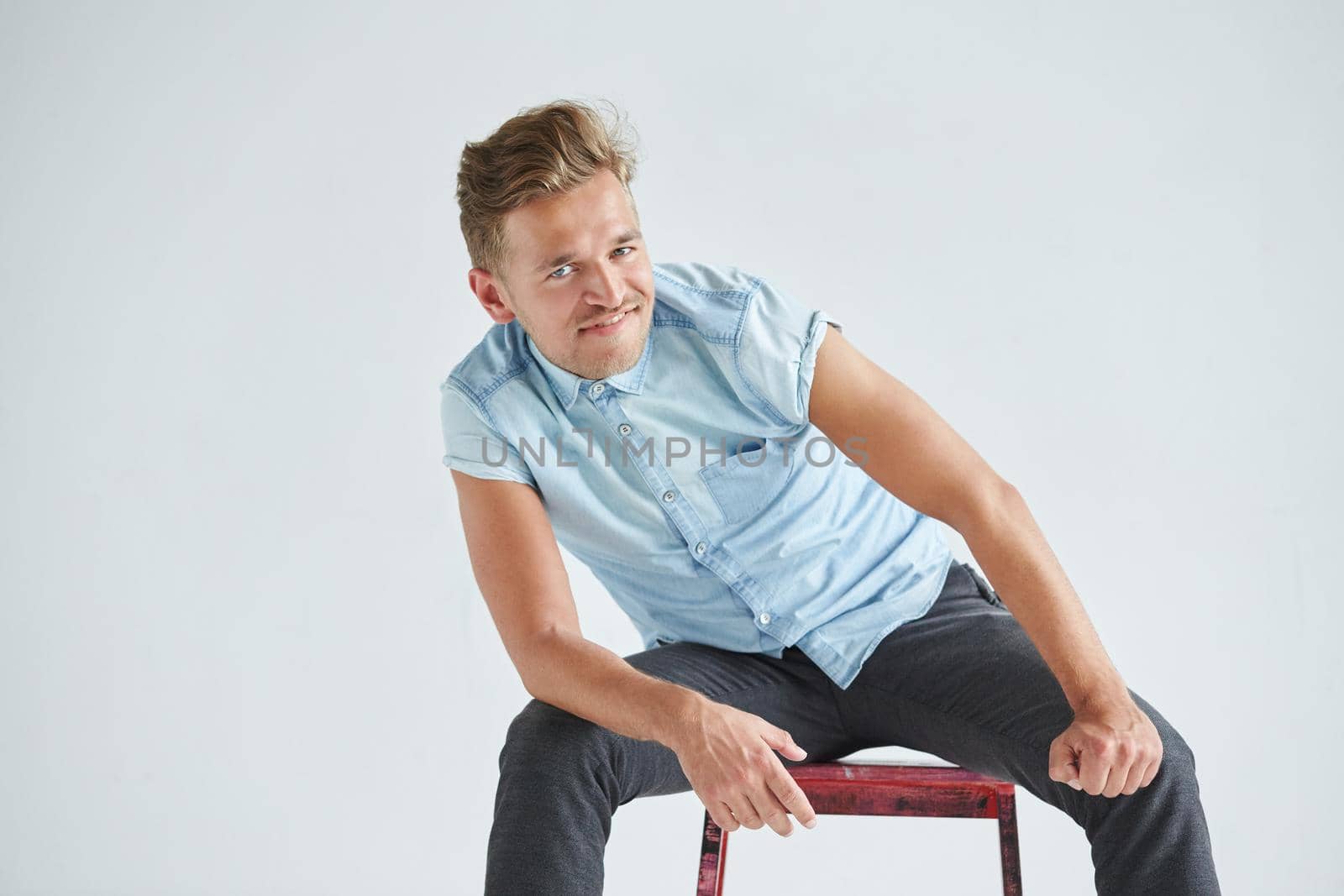 Brutal man in a shirt with short sleeves sitting in the chair, his fists clenched, slightly bent, under the gaze of the forehead. High quality photo