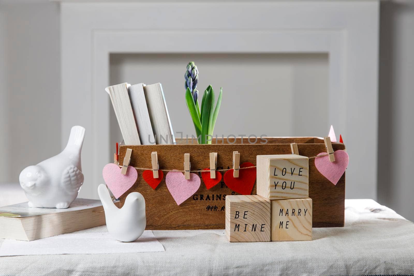 Wooden container with books, three cubes on the table against the background of a white fireplace. Place for text. Valentine's Day