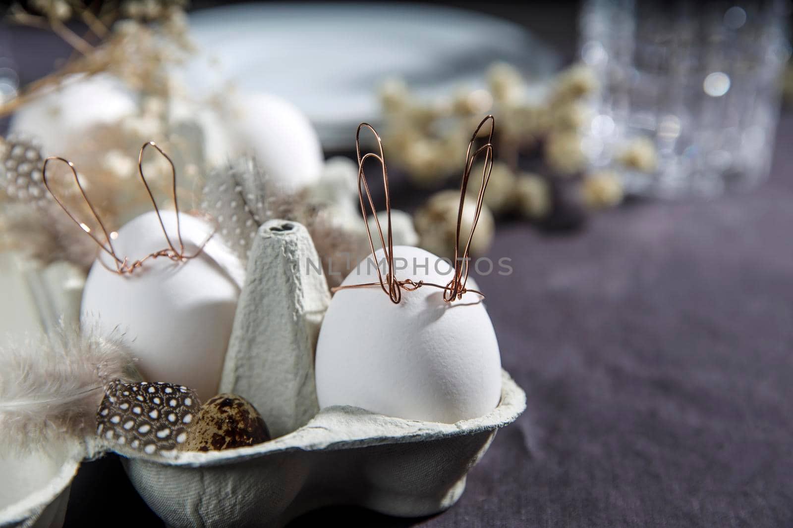 Easter concept. A white egg with copper wire ears and a painted rabbit sleeping face in a box. Partridge eggs and feathers.