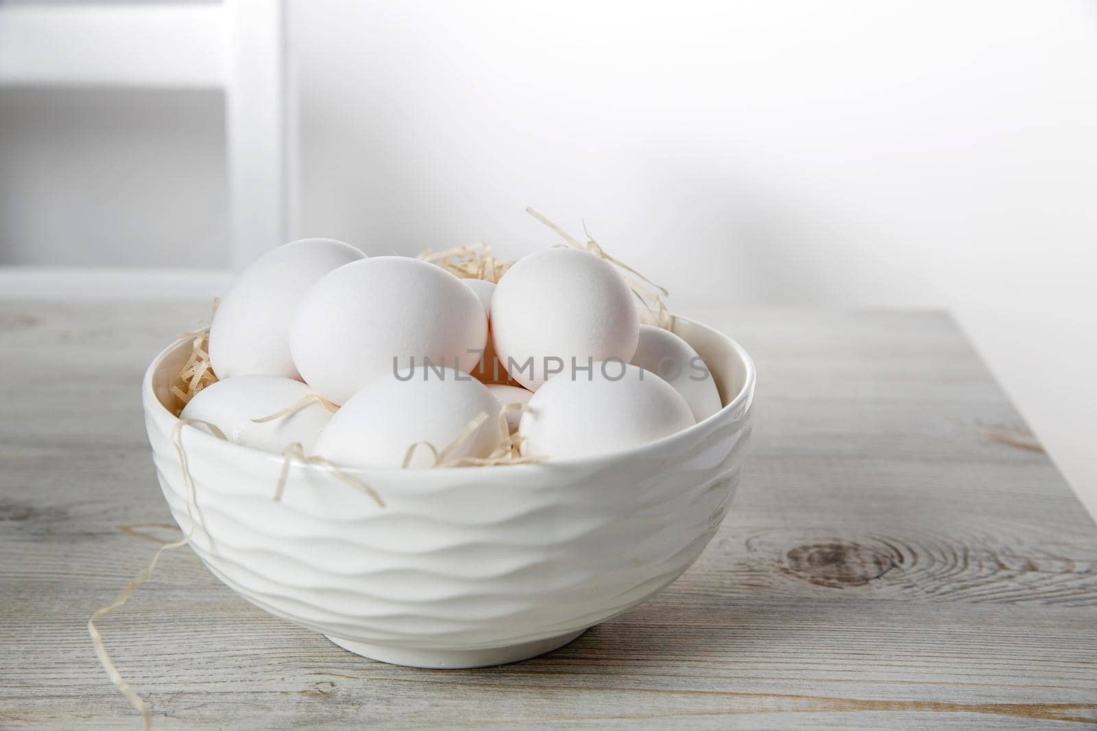 Patterned bowl with eggs on beige wooden table in white scandinavian style kitchen. Place for text. Copy space