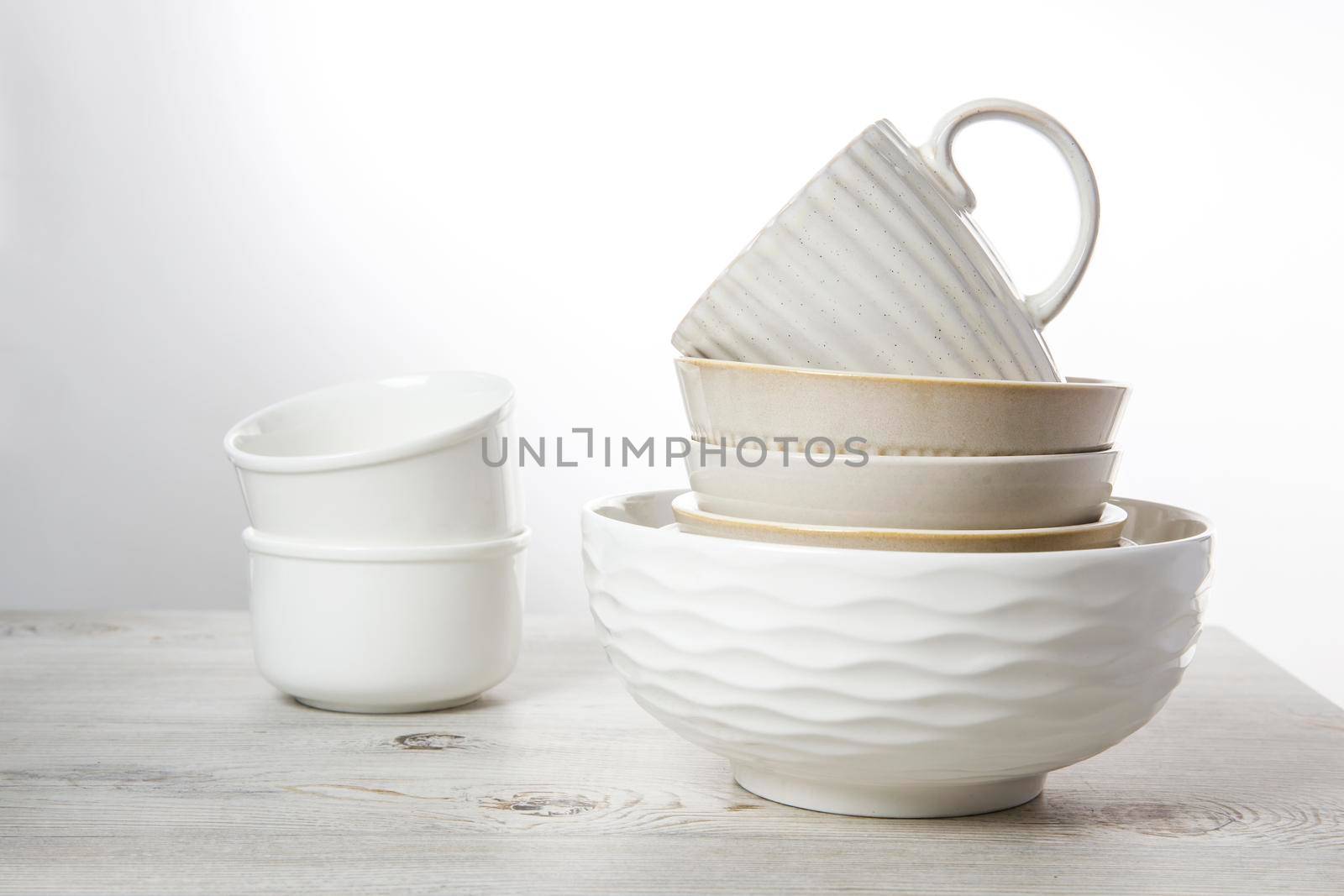 A pyramid of white bowls, plates and cups of different sizes and colors on a beige table in the kitchen. Scandinavian style. Place for your text. Copy space by elenarostunova