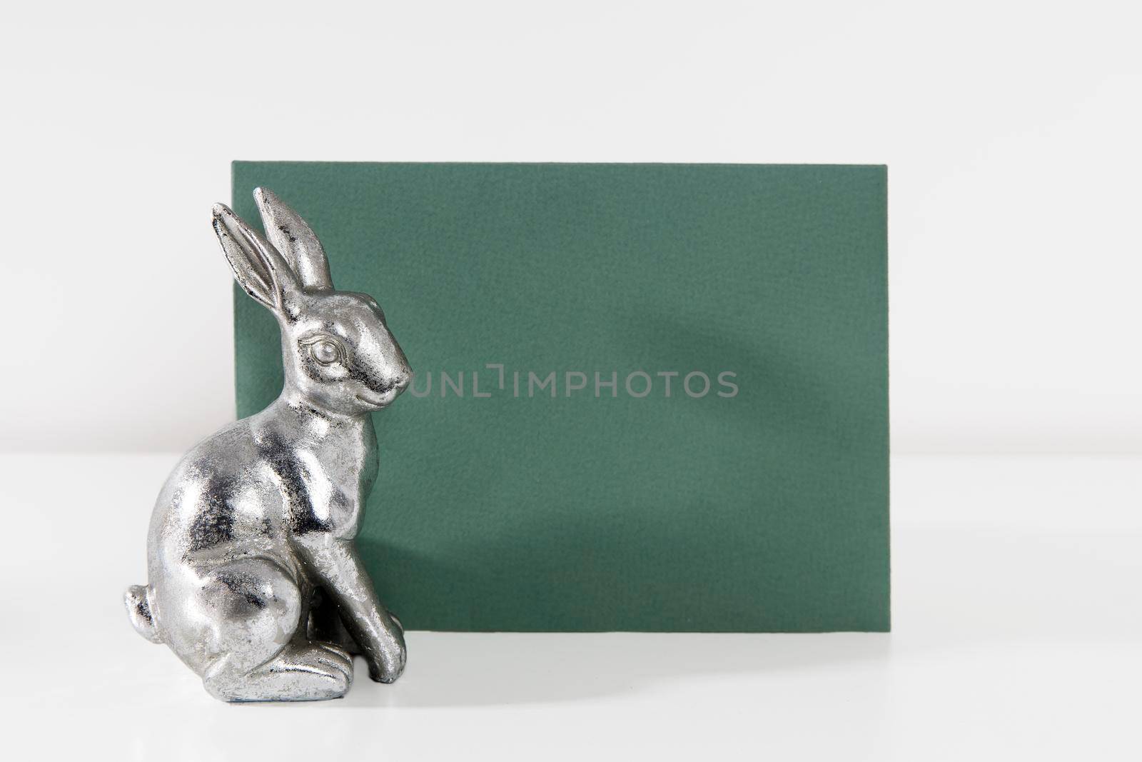 Mock up white frame with modern ceramic easter bunny decor with green card on a shelf. White color scheme. Landscape frame orientation.
