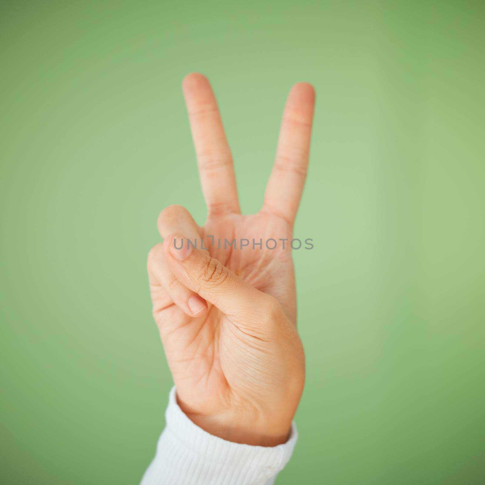 were head bumping to positivity. Shot of an unrecognizable woman showing the peace sign against a green background. by YuriArcurs