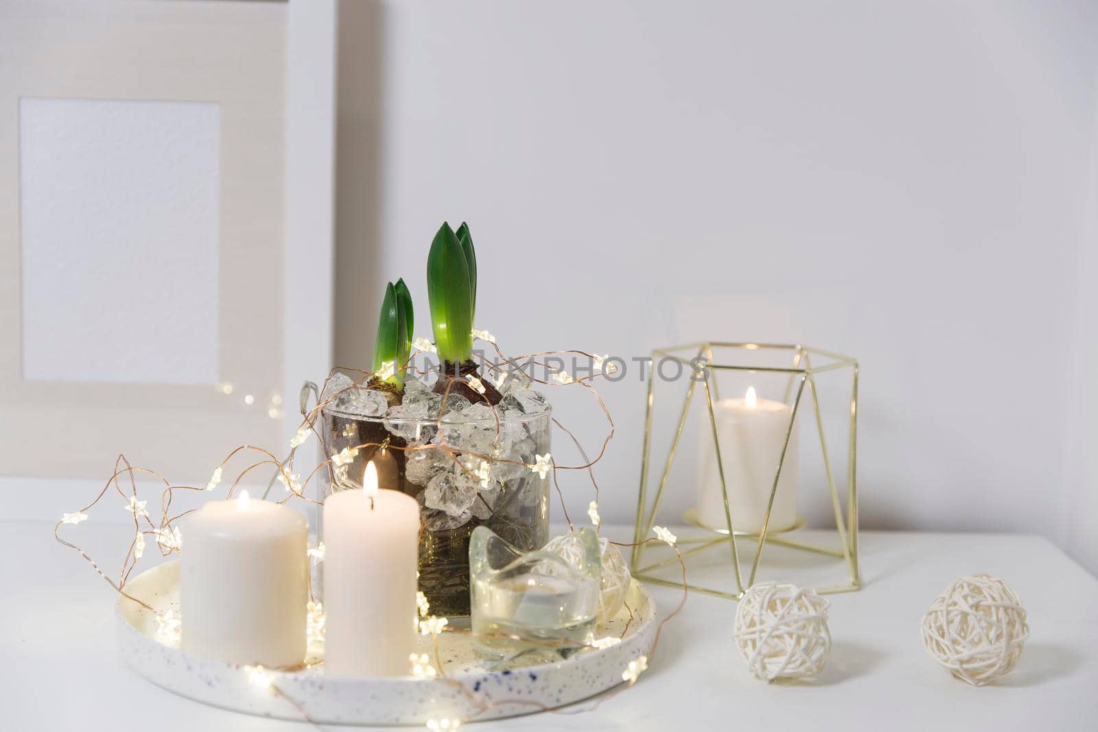 Two unopened hyacinths in a glass vase with artificial ice. Interior view in modern scandinavian style with painting canvas or poster on the wall. Living room, chest of drawers with vases.