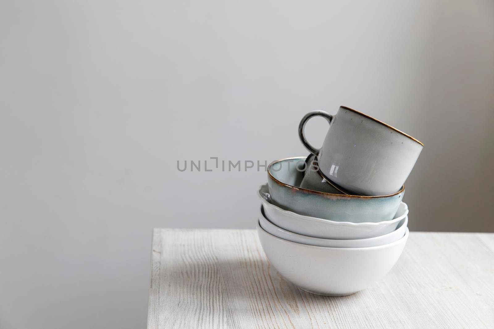 A pyramid of white bowls, plates and cups of different sizes and colors on a beige table in the kitchen. Scandinavian style. Place for your text. Copy space by elenarostunova