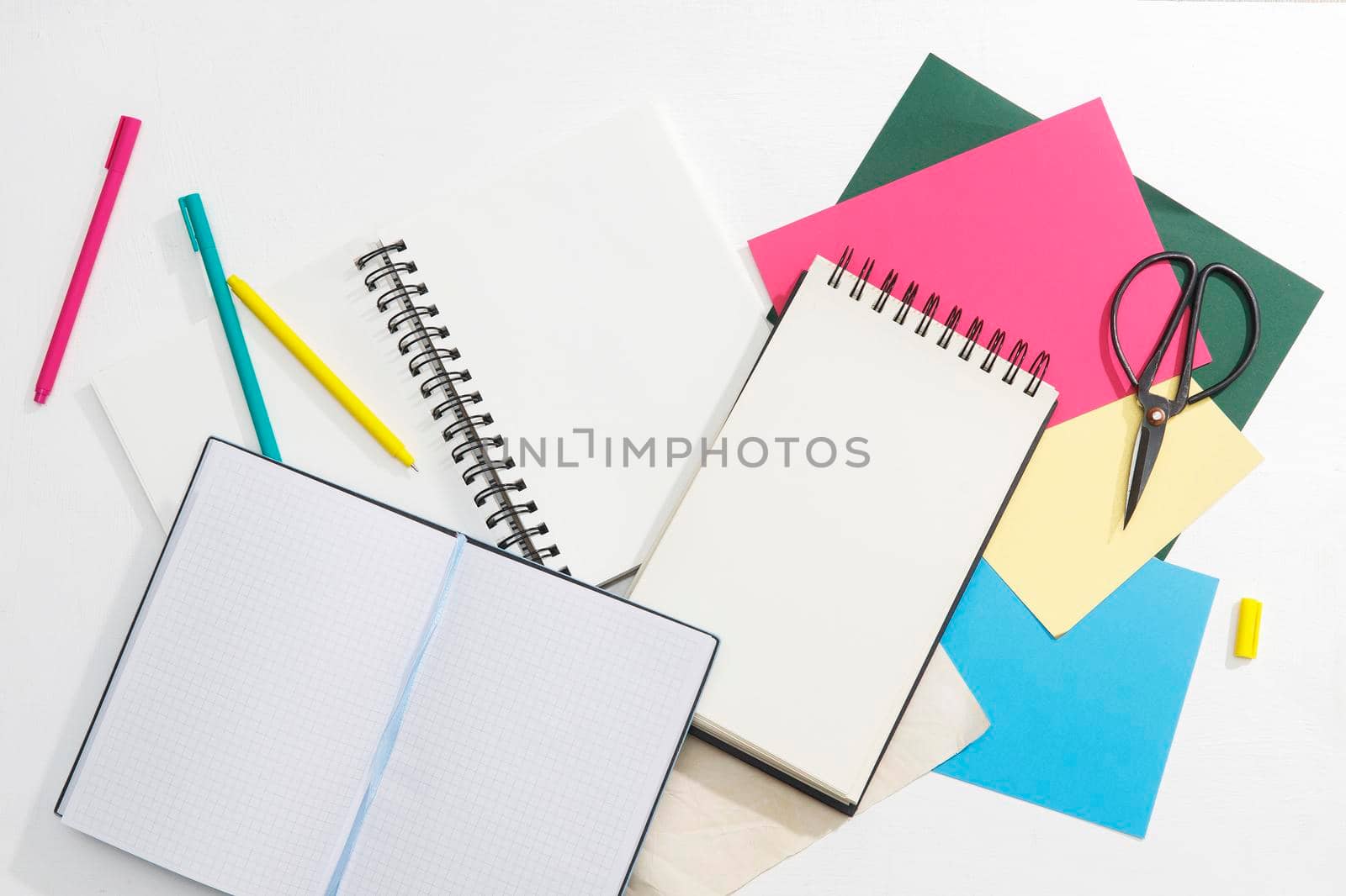 A lot of notebooks on springs, multi-colored paper: blue, red, green, gold, pens and scissors. Office concept. Place for text