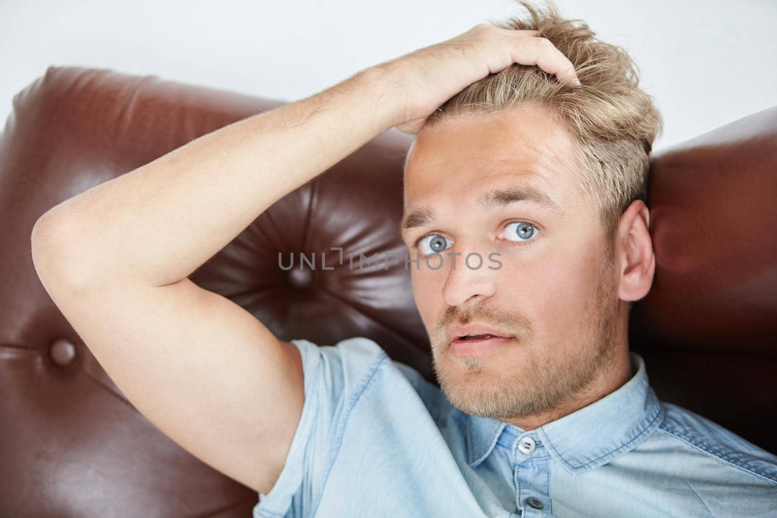 Brutal man in a shirt with short sleeves sitting in the brown chair , holding hand behind the head, close up portrait. High quality photo