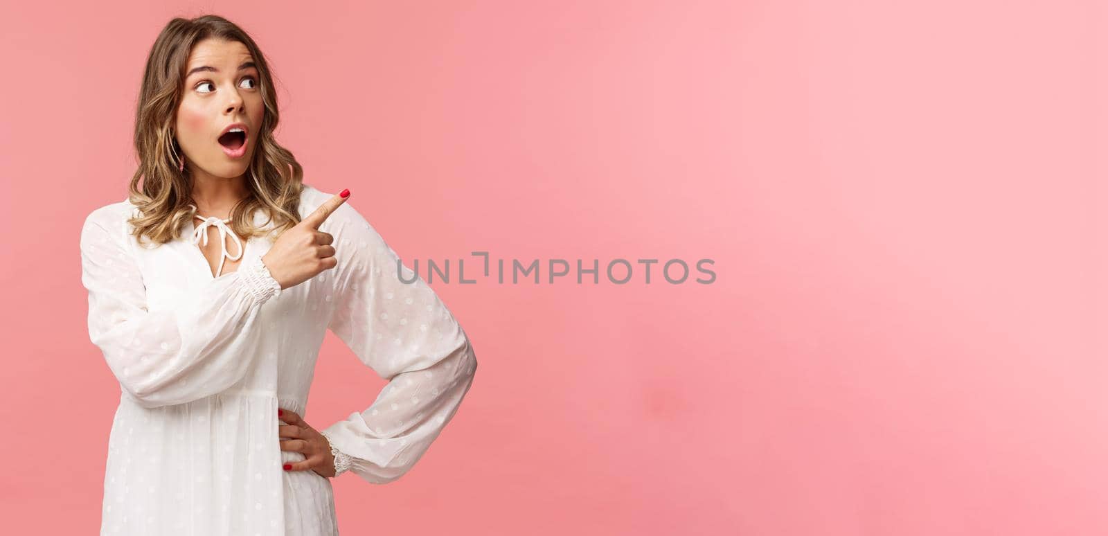 Surprised and excited good-looking blond girl in white cute dress, open mouth in amazement, look curious pointing upper right corner astonished, see something awesome, pink background by Benzoix