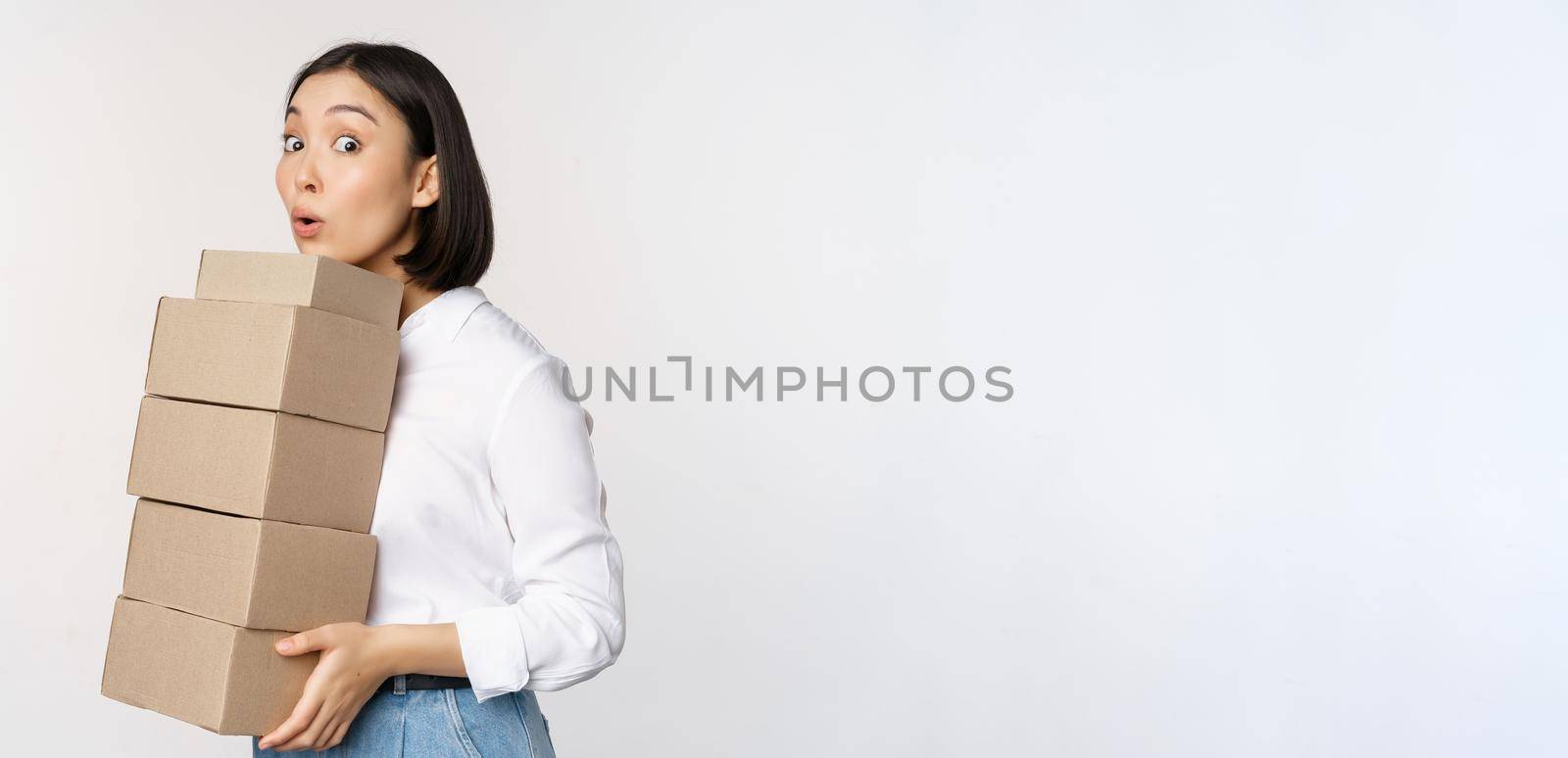 Portrait of young asian woman holding boxes, carry delivery goods. Korean female entrepreneur assemble order, standing voer white background.