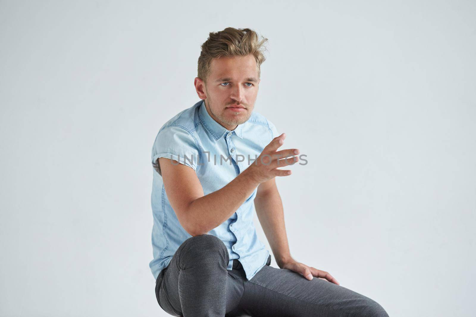 Brutal man in a shirt with short sleeves sitting in the chair , his fists clenched , slightly bent , under the gaze of the forehead. High quality photo