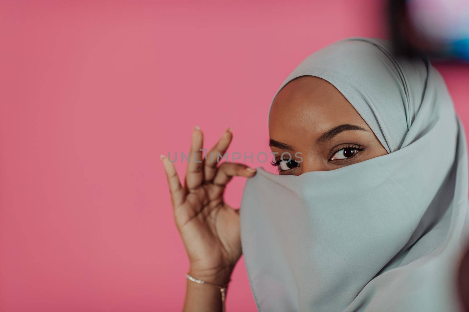 Portrait of young modern muslim afro beauty wearing traditional islamic clothes on plastic pink background. Selective focus. High quality photo