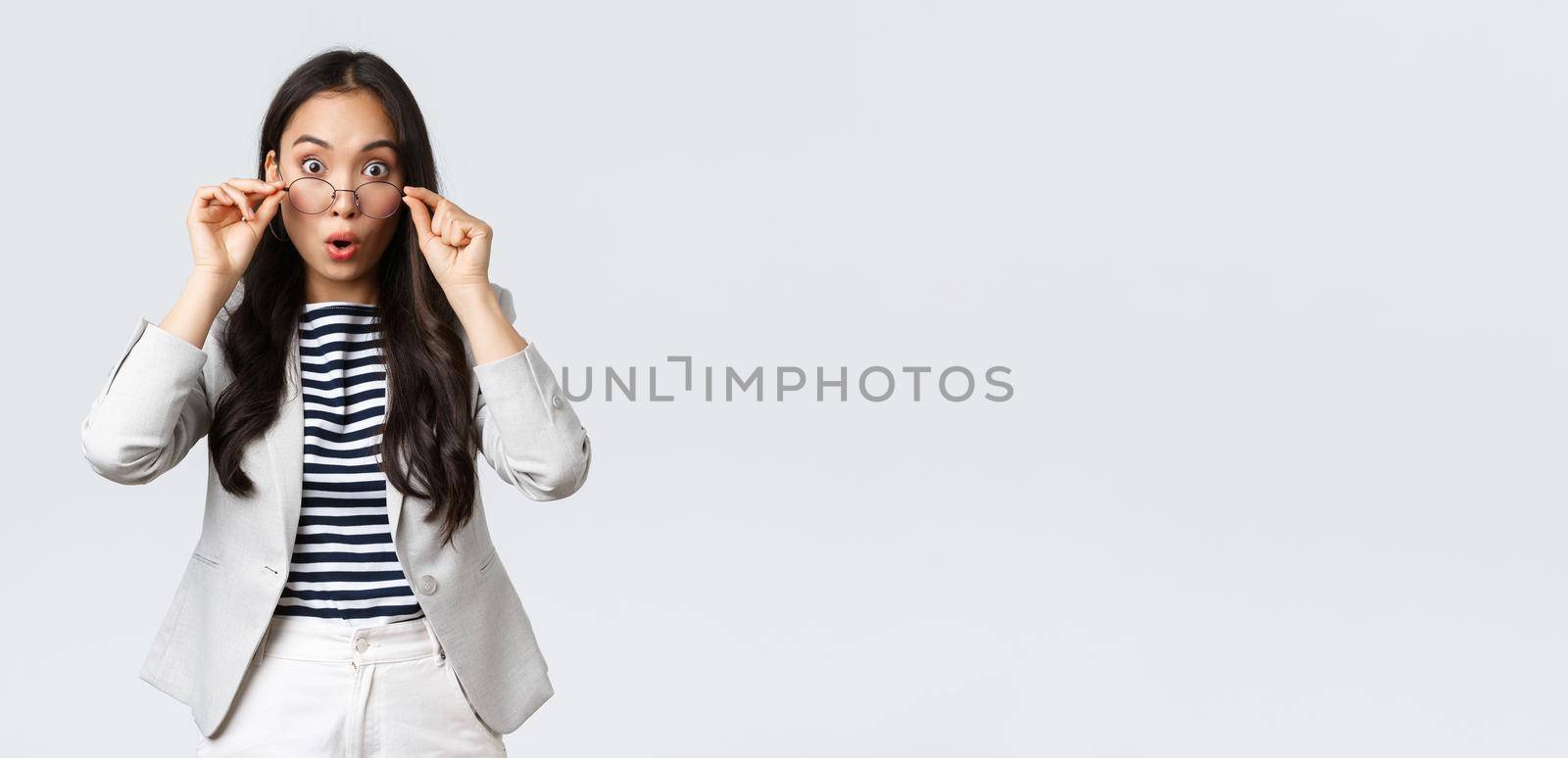 Business, finance and employment, entrepreneur and money concept. Shocked asian office lady take-off glasses and widen eyes as hear big news, gasping amazed, stand white background.