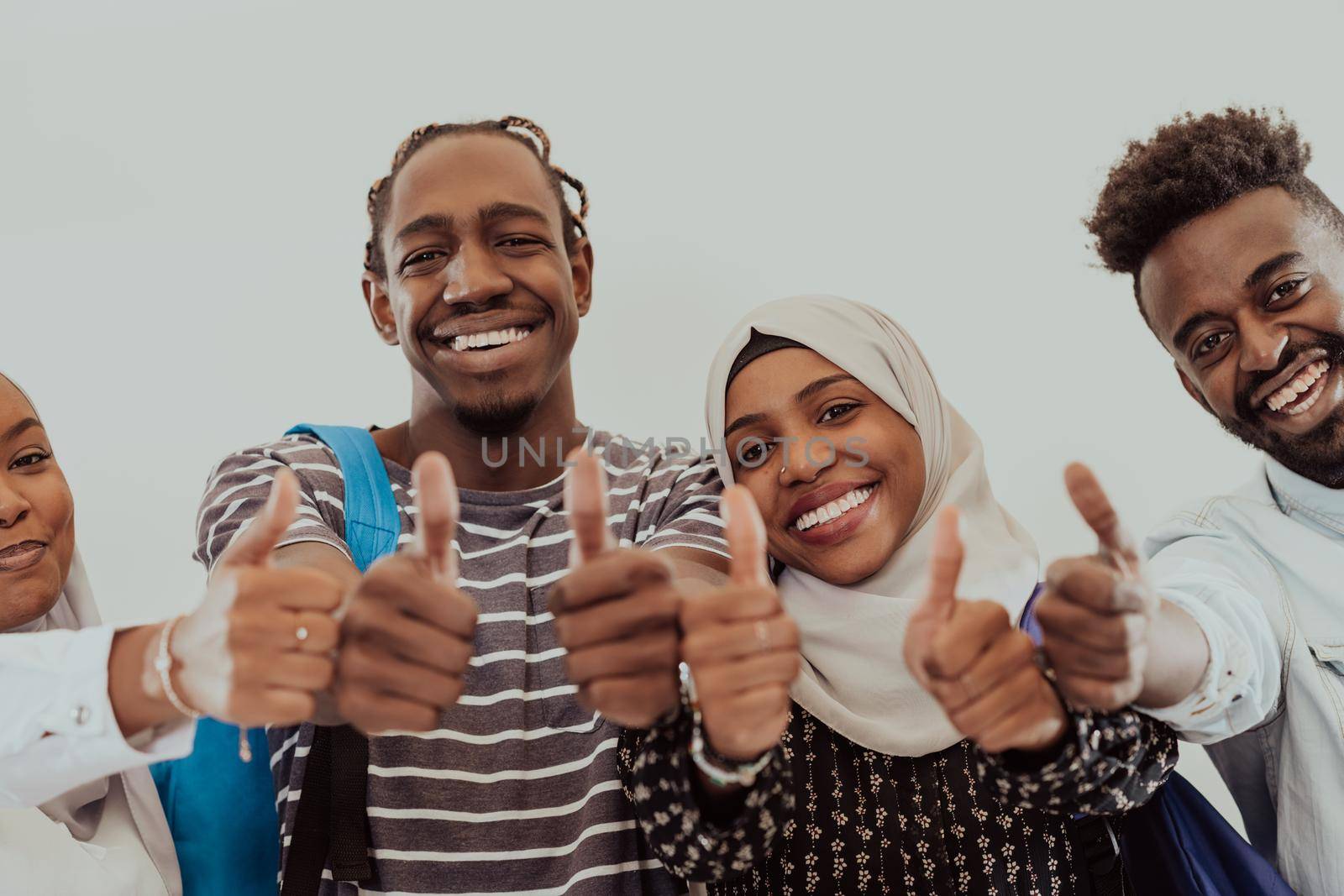Group portrait of happy African students standing together against a white background and showing ok sign thumbs up girls wearing traditional Sudan Muslim hijab fashion by dotshock