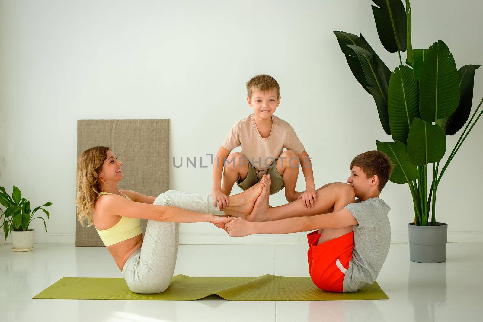 Sports happy family, a slim woman, a boy and teenager perform group yoga exercises with support while sitting on a sports mat. copy space