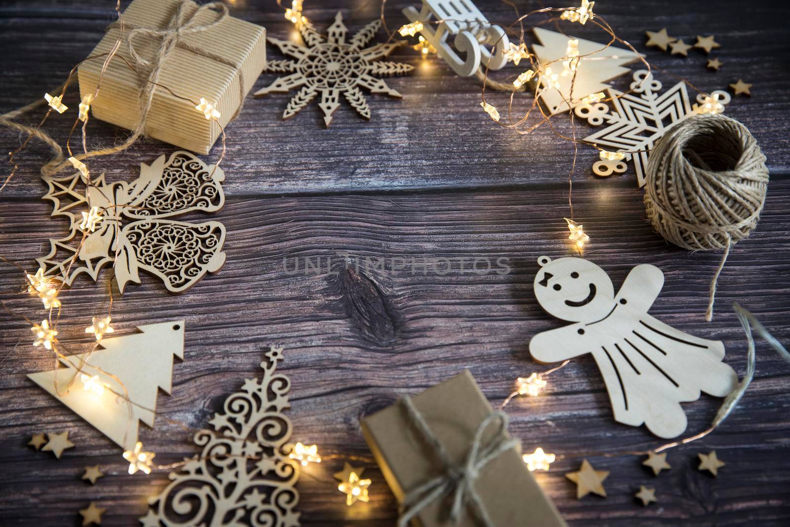 Glowing garland star, two gray boxes with gifts tied with twine, plywood Christmas decorations carved from wood on a wooden table surface. Copy space by elenarostunova