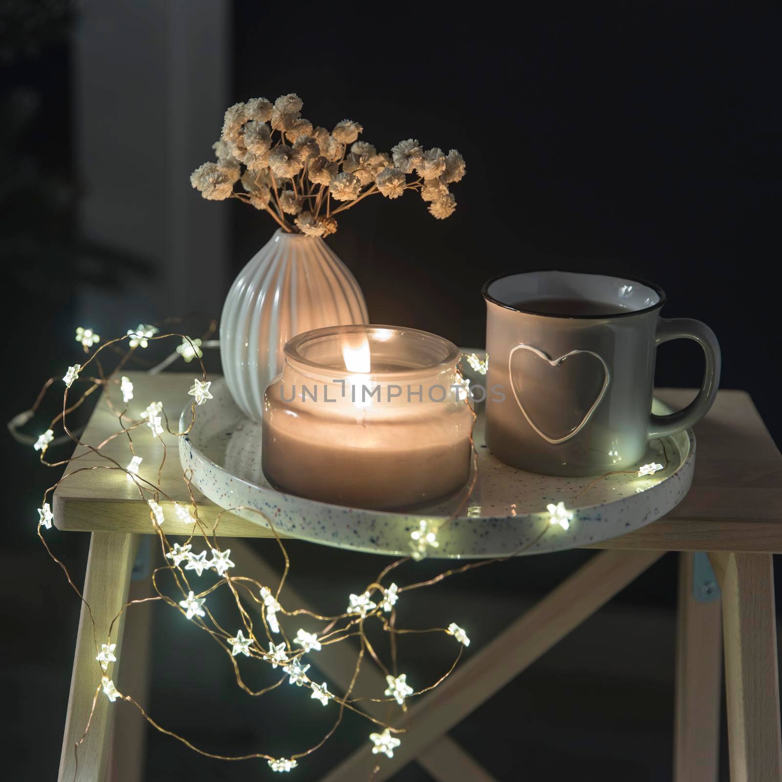 A vase with white dry flowers, a gray enamel cup with a drawn heart with tea, a burning candle stand on a tray for Valentine's Day. Copy space. Place for text.