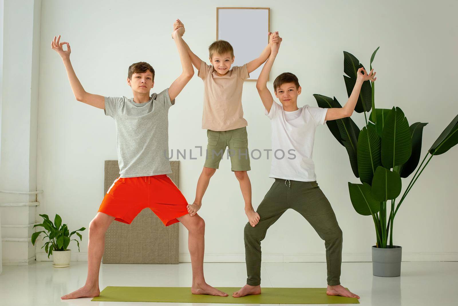 a happy boy and two teenagers perform group yoga exercises with support while sitting on a sports mat. copy space