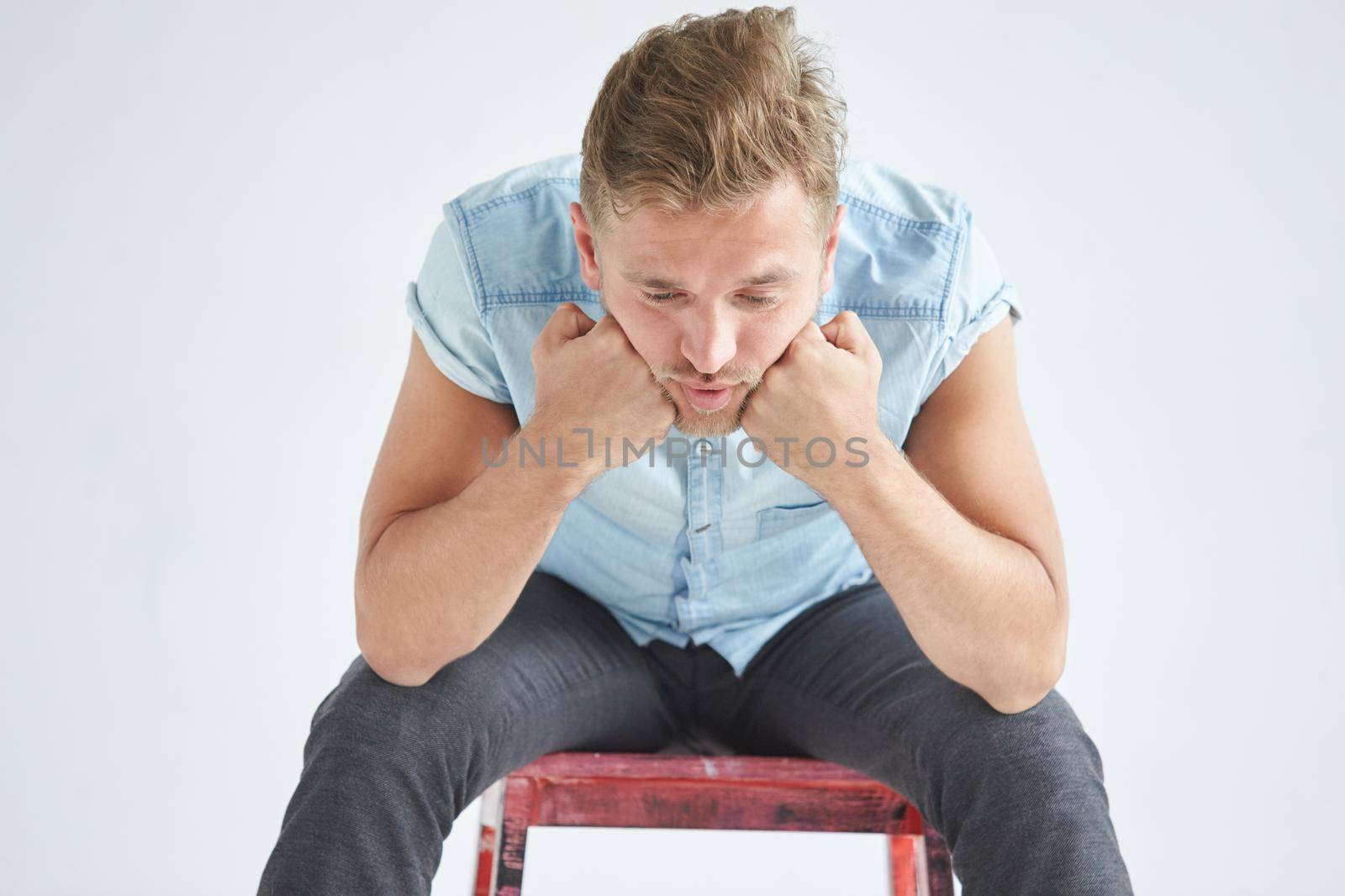 Brutal man in a shirt with short sleeves sitting in the chair , his fists clenched , slightly bent , under the gaze of the forehead. High quality photo