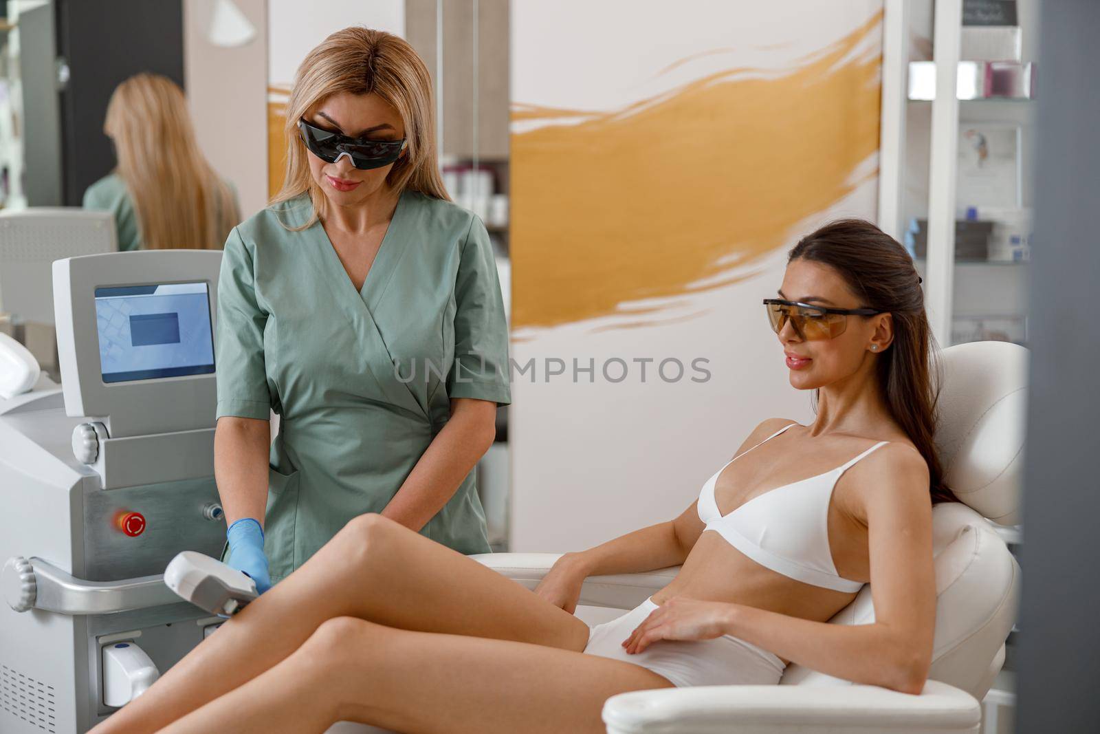 Hair removal procedure on legs in beauty salon, two women. Photo epilation concept