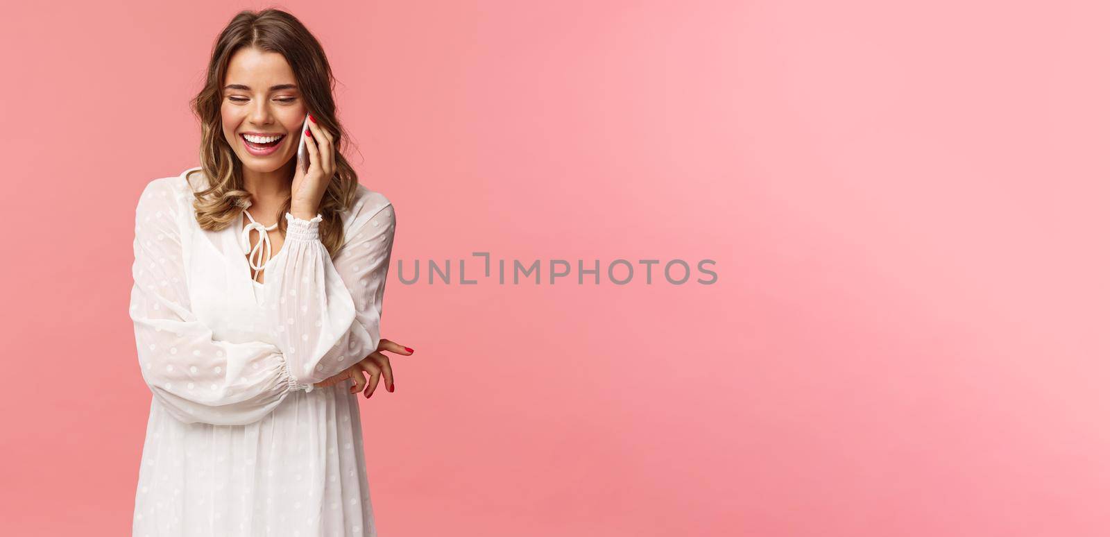 Communication and technology concept. Attractive caucasian female in white dress, blond short haircut, hold smartphone, talking on mobile phone and laughing, smiling carefree, pink background by Benzoix