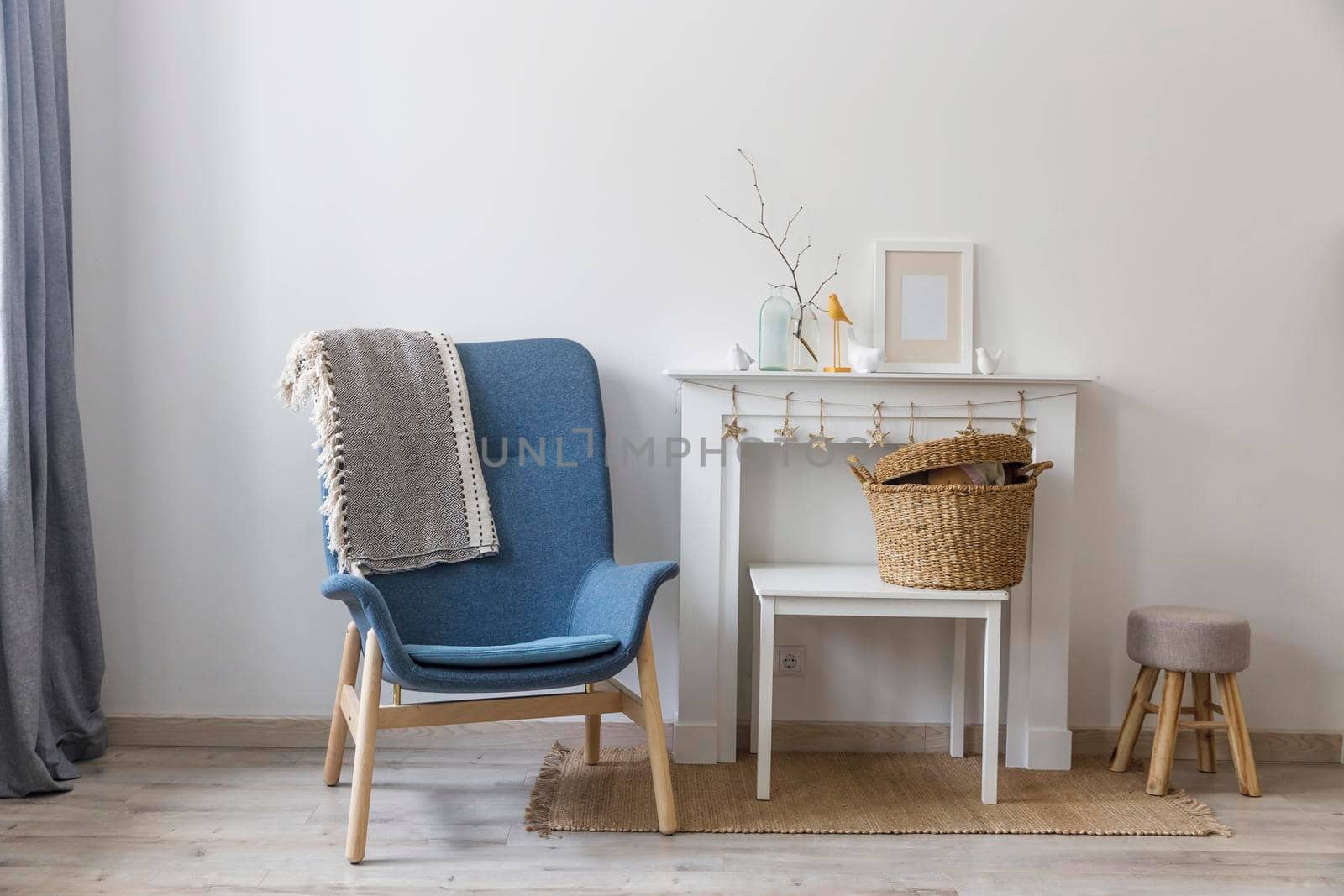 Fragment of the interior of a cozy house. A gray armchair by a white fireplace. On the fireplace is a glass bottle with a branch, figurines of birds and a photo frame. Place for text by elenarostunova