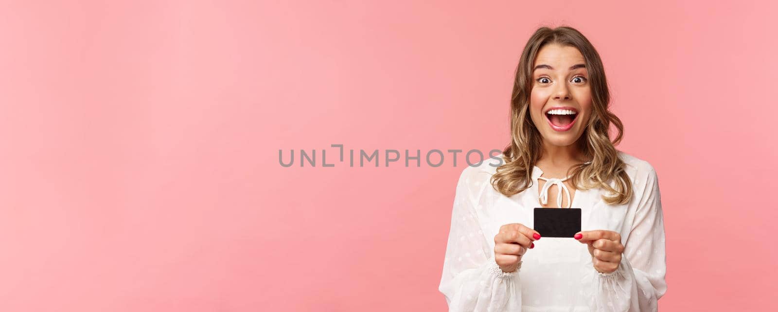 Close-up portrait of excited and happy good-looking blond female recommend bank, smiling amazed, holding credit card, paying for purchase, shopaholic in store feel upbeat.