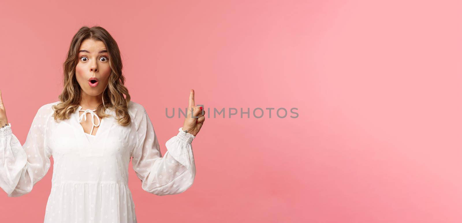 Waist-up portrait of amazed blond girl say wow in excitement, pointing fingers up, showing person top advertisement with cool special spring discount, standing pink background by Benzoix