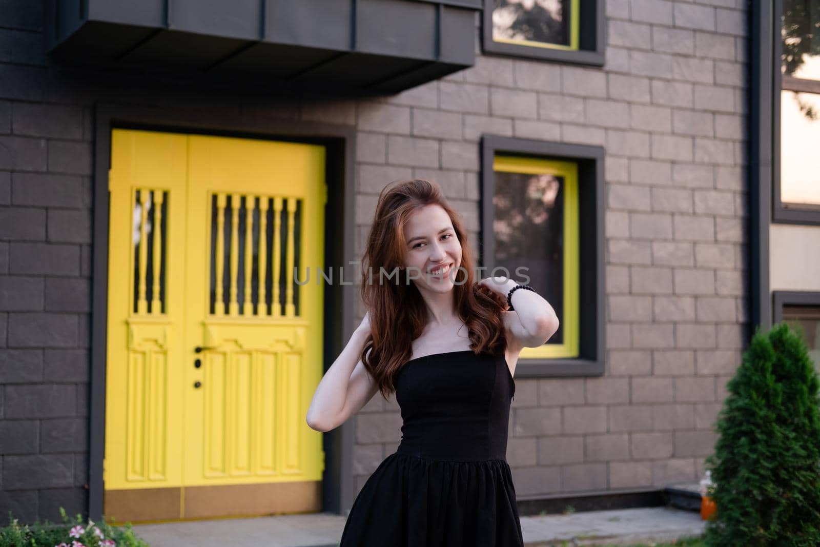 happy young woman in a black dress in front of modern building with yellow door. housewarming. buying a house. happy life in private house. new home.