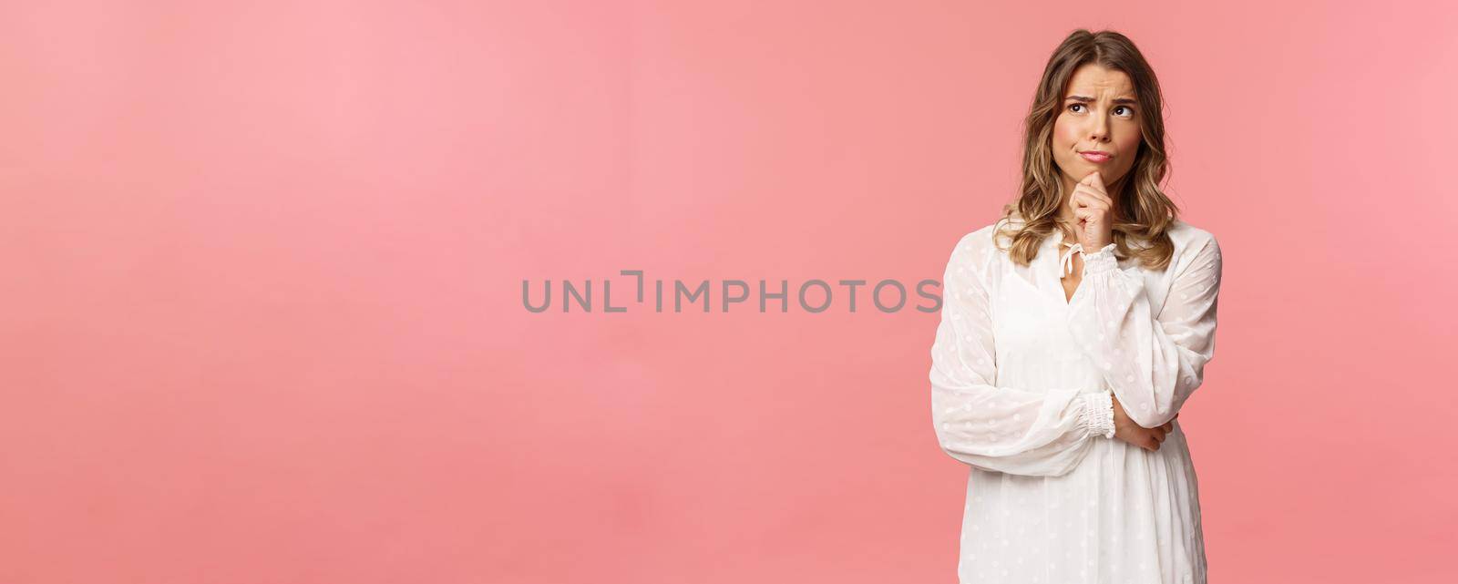 Beauty, fashion and women concept. Portrait of uncertain, serious-looking feminine young blond woman in white dress, touch chin, smirk and frowning thoughtful, look away thinking by Benzoix