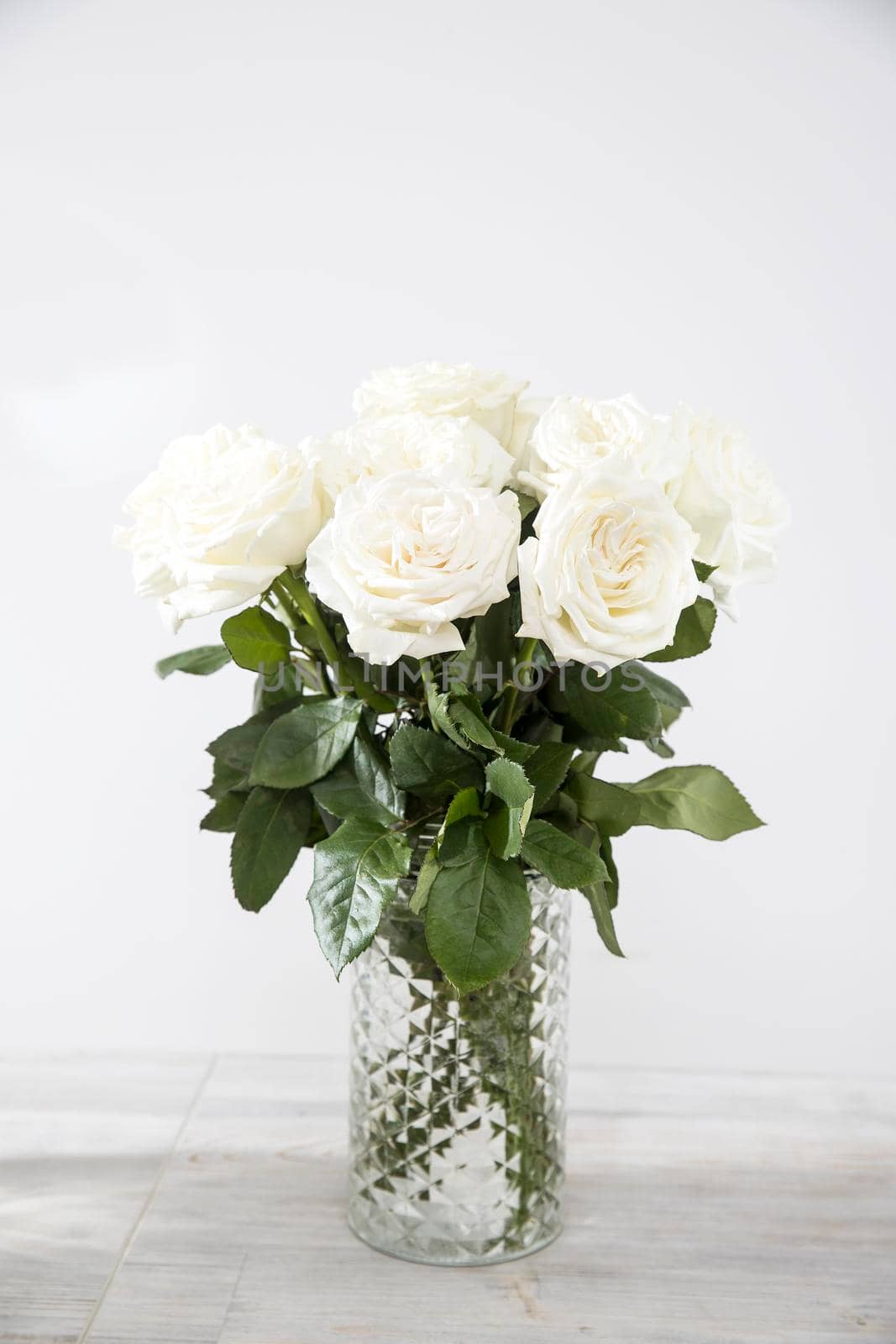 Bouquet of white roses in a glass vase on a beige table against a gray wall. Copy space. A place for text.