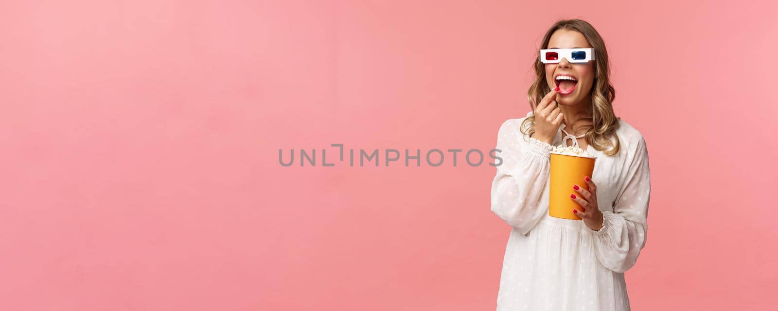 Leisure, going-out and spring concept. Portrait of attractive young woman in white dress enjoying watching interesting movie on full screen at cinema, eating popcorn and wearing 3d glasses by Benzoix