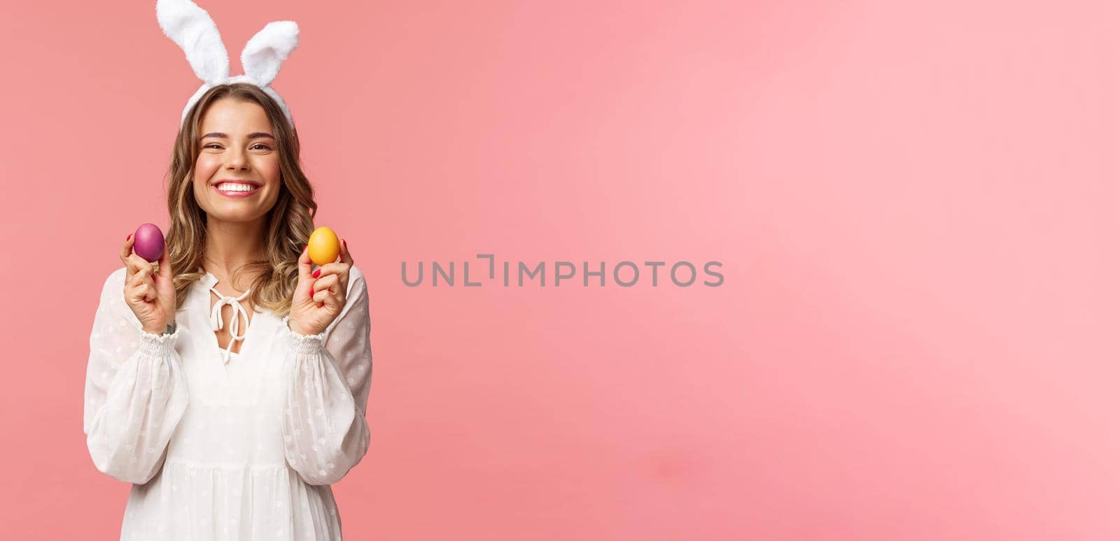 Holidays, spring and party concept. Portrait of lovely, cheerful blond girl in rabbit ears, holding colored eggs, celebrating Easter with family, enjoying spend traditional day with close people.