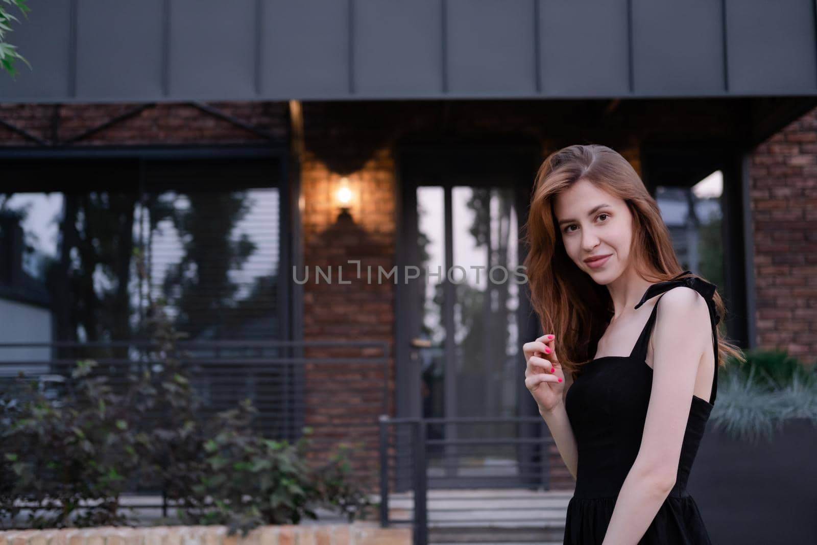 confident single woman near her new home. brown and black modern building. happy carefree suburb life.