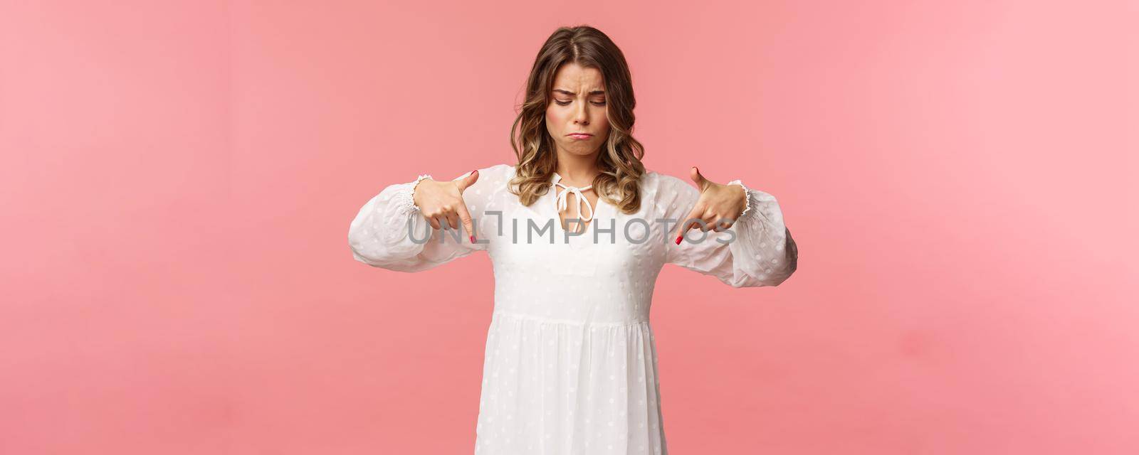 Gloomy, jealous and upset cute blond european woman in white trendy spring dress, sulking as pointing and looking down, see something expensive, cant efford it, strand pink background by Benzoix