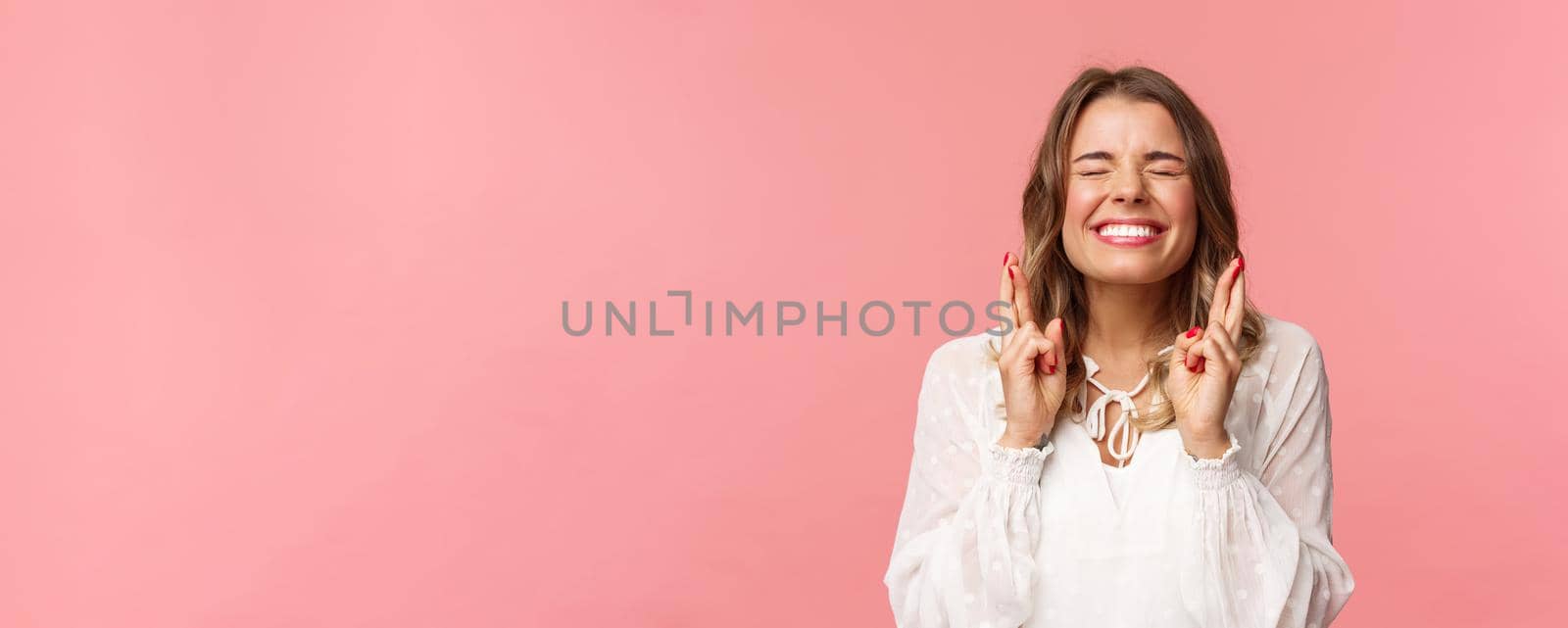 Portrait of excited hopeful blond girl making wish crossed fingers for good luck, close eyes and smiling putting all effort into pray, pleading for dream come true, anticipating over pink background by Benzoix