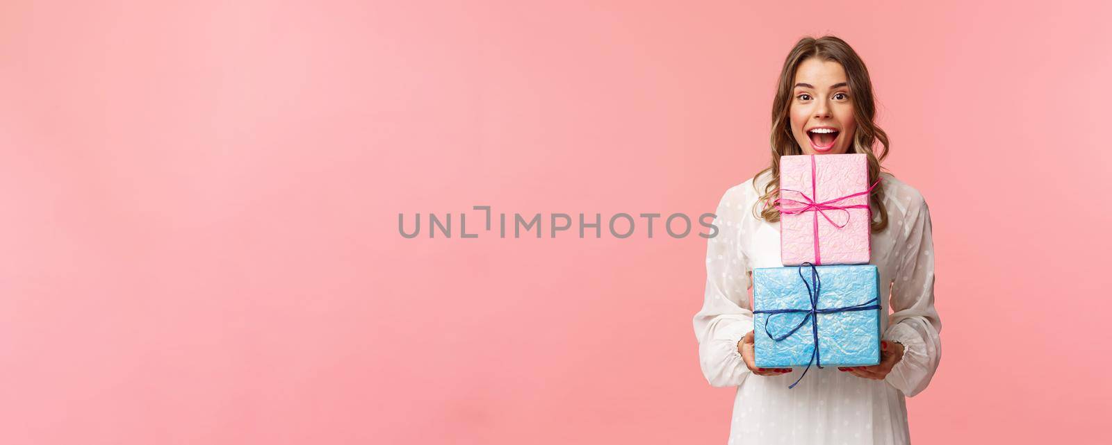 Holidays, celebration and women concept. Portrait of happy cheerful girl likes celebrating birthday and receive presents, holding two gift boxes and smiling camera, pink background.