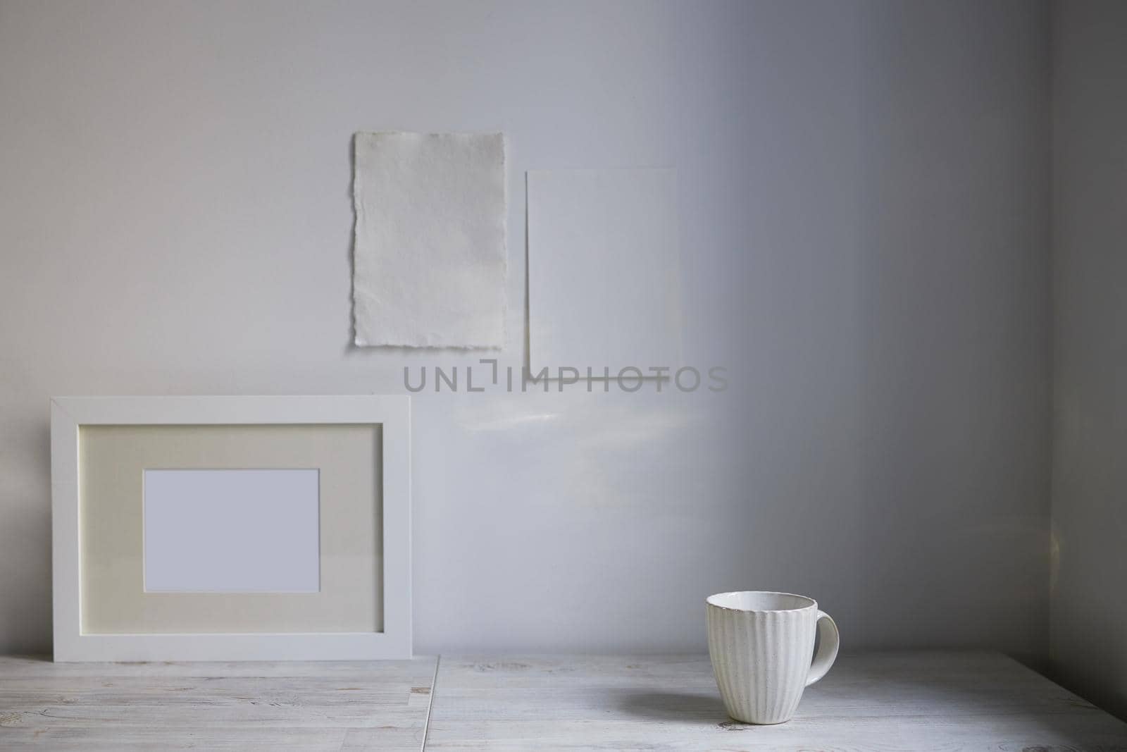 Scandinavian style. Interior Design. A white cup, , a frame for a photo are on the table. Two blank sheets of paper are attached to the wall. Empty space for text