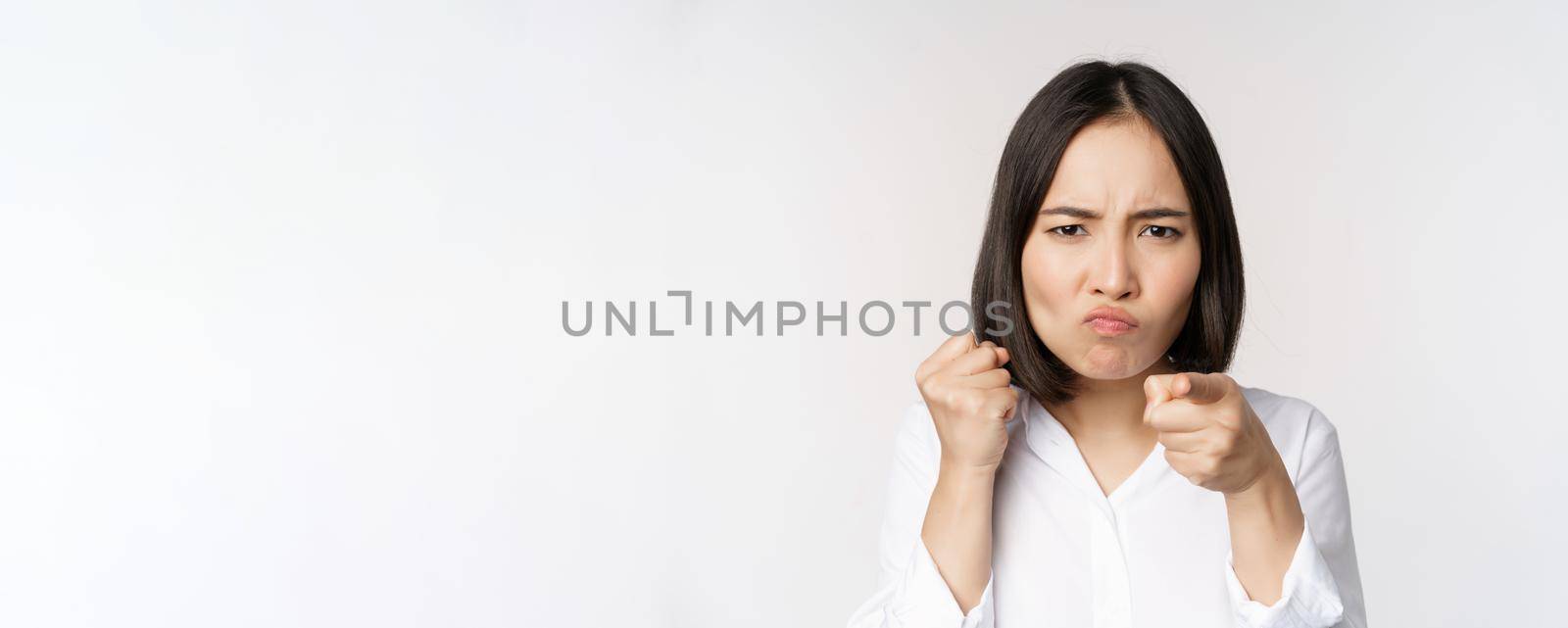 Close up of angry young woman clench fists, ready for fight, fighting, standing over white background.