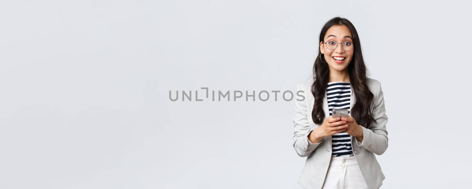 Business, finance and employment, female successful entrepreneurs concept. Cheerful happy asian businesswoman, office manager looking upbeat camera with smile, using smartphone by Benzoix