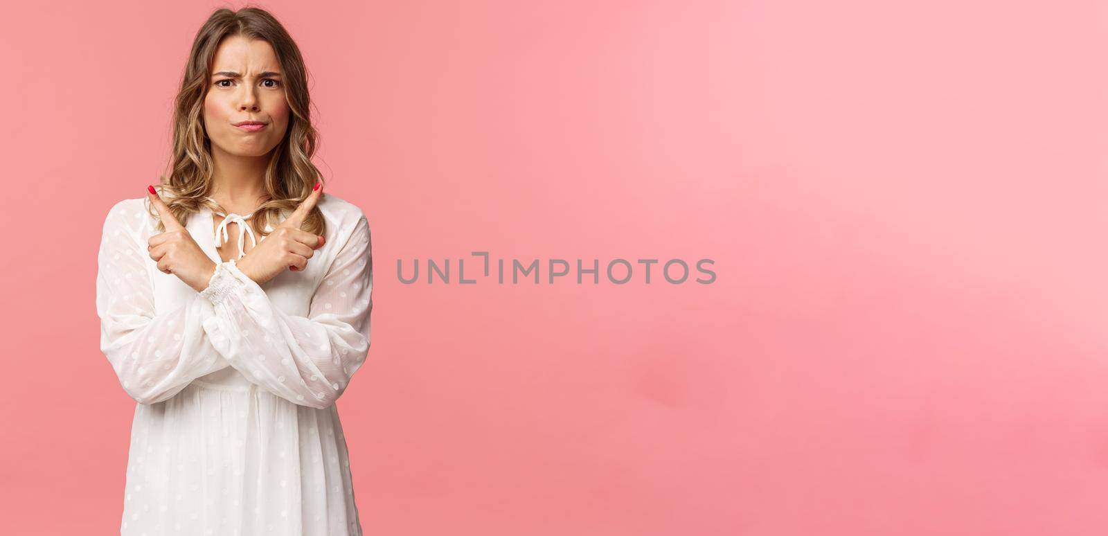 Beauty, fashion and women concept. Portrait of troubled blond girl in white dress need advice, trying make choice, smirk and frown puzzled, pointing left and right two variants, pink background.