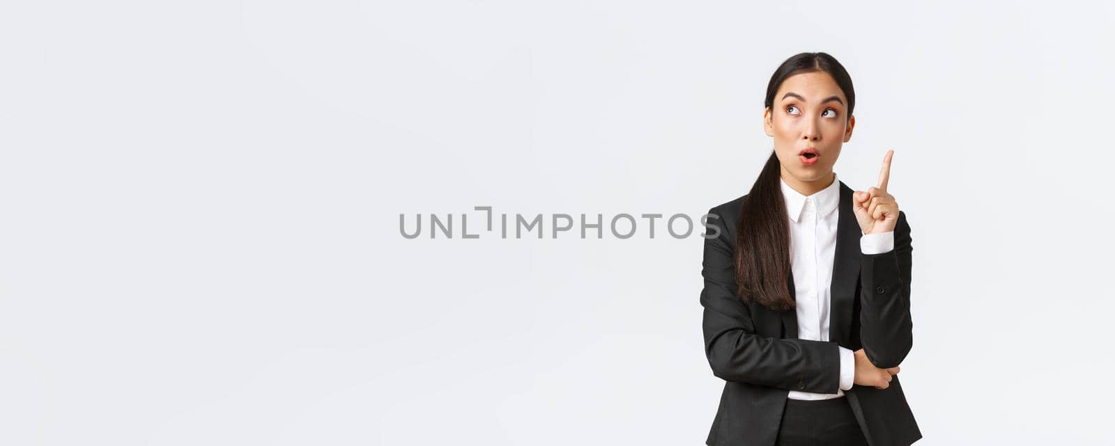 Smart and creative asian businesswoman have excellent idea, raising finger up and looking upper left corner thoughtful, suggest solution, make plan, saying thought over white background by Benzoix