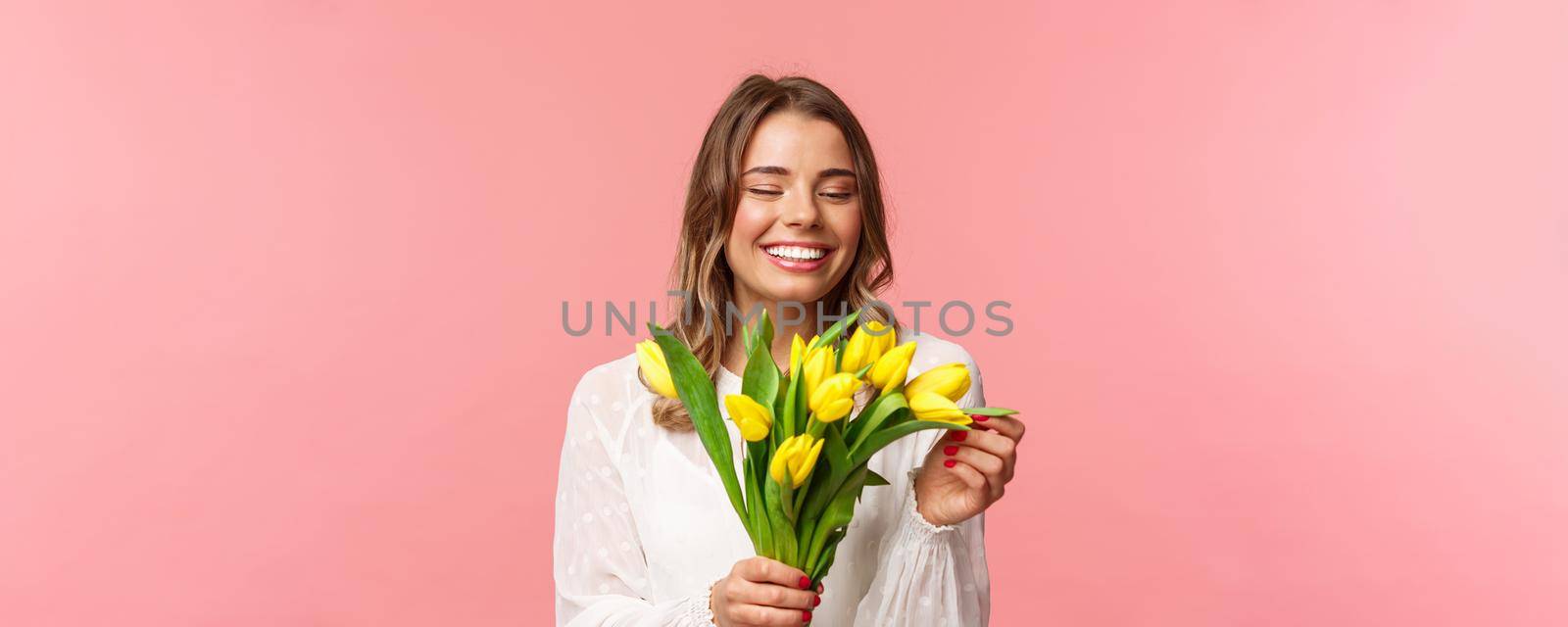 Spring, happiness and celebration concept. Close-up portrait of lovely romantic smiling girl touching petal of yellow tulip, holding flowers, receive bouquet on date, standing pink background by Benzoix